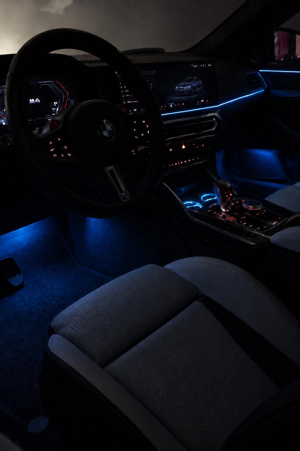 Interior de un BMW M4 de noche con el Pack Noche Express encendido en azul: línea de luz en el salpicadero, luces de pies y posavasos LED