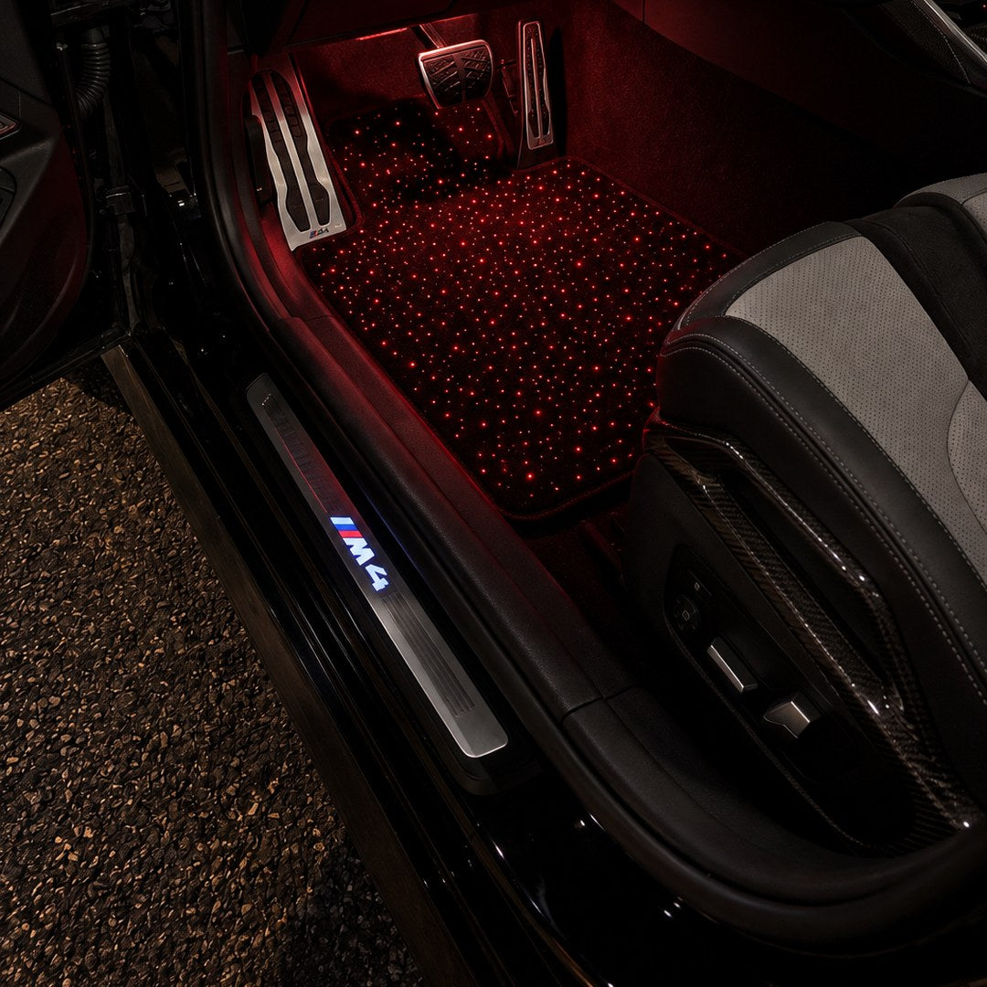 Alfombrillas de cielo estrellado encendidas en rojo en un BMW M4 de noche con la puerta abierta
